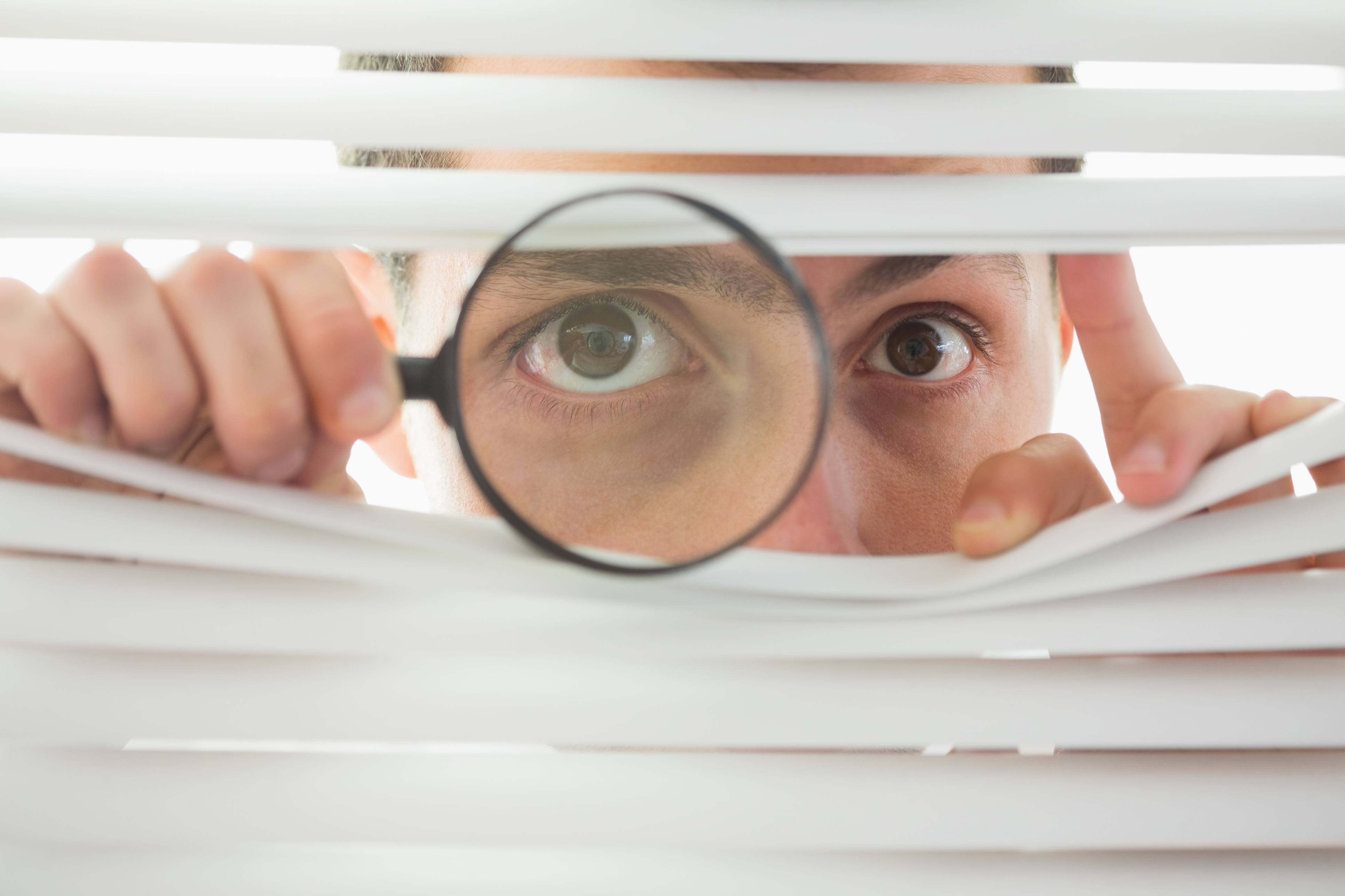 Male eyes spying through roller blind with loupe