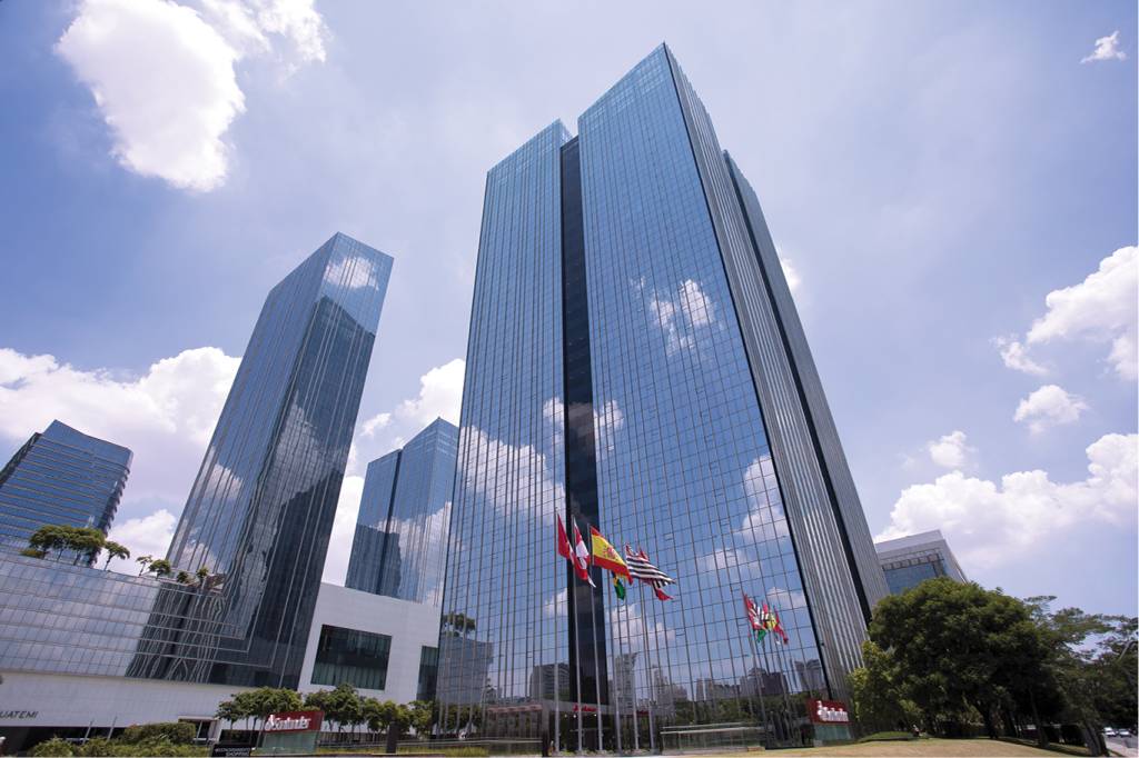 Fachada de um prédio espelhado na região da Faria Lima. Em frente, bandeiras de São Paulo, Brasil e Espanha.