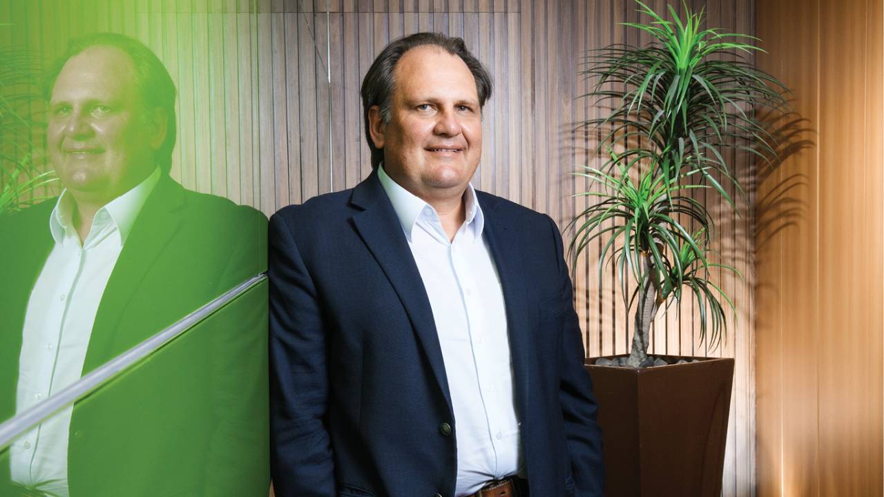 Foto do presidente da empresa, que posa ao lado de um painel verde
