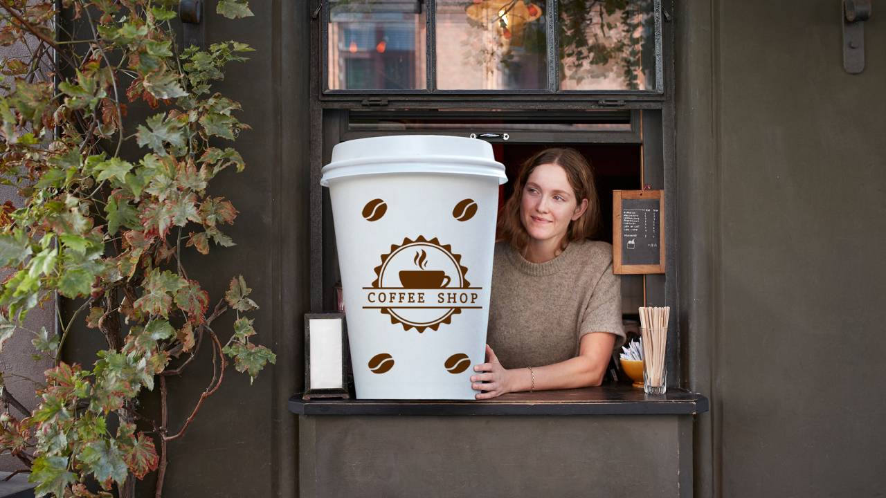 Mulher serve copo de café gigante com logotipo da cafeteria.