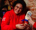 Menina negra posa de frente, sorrindo para a foto. Em suas mãos, uma coxinha com maionese Heinz.