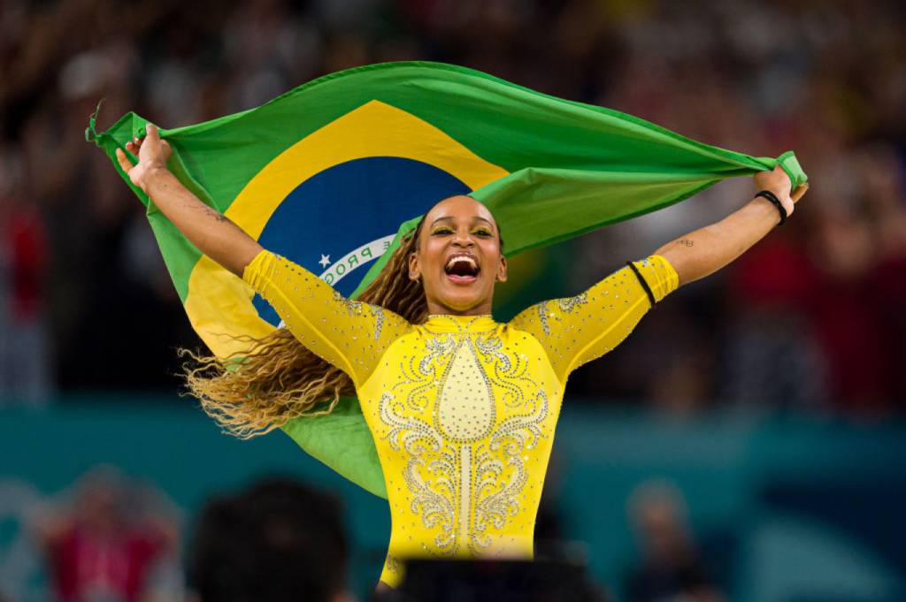 Sofia_Esteves_olimpiadas_trabalho_equipe_02_layout_site A medalhista de prata Rebeca Andrade, do Time Brasil, comemora com a bandeira brasileira após competir na final do individual geral feminino de ginástica artística no sexto dia dos Jogos Olímpicos de Paris 2024, na Bercy Arena, em 1º de agosto de 2024, em Paris, França.