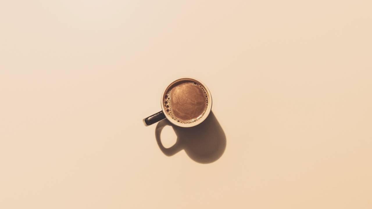 Xícara de café vista de cima, preenchida com o líquido. O fundo é bege.