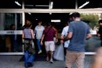 A imagem mostra um grupo de pessoas entrando por uma porta de vidro em um prédio com a inscrição 