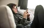 Foto de um adolescente mexendo no celular enquanto esta sentado no sofa.