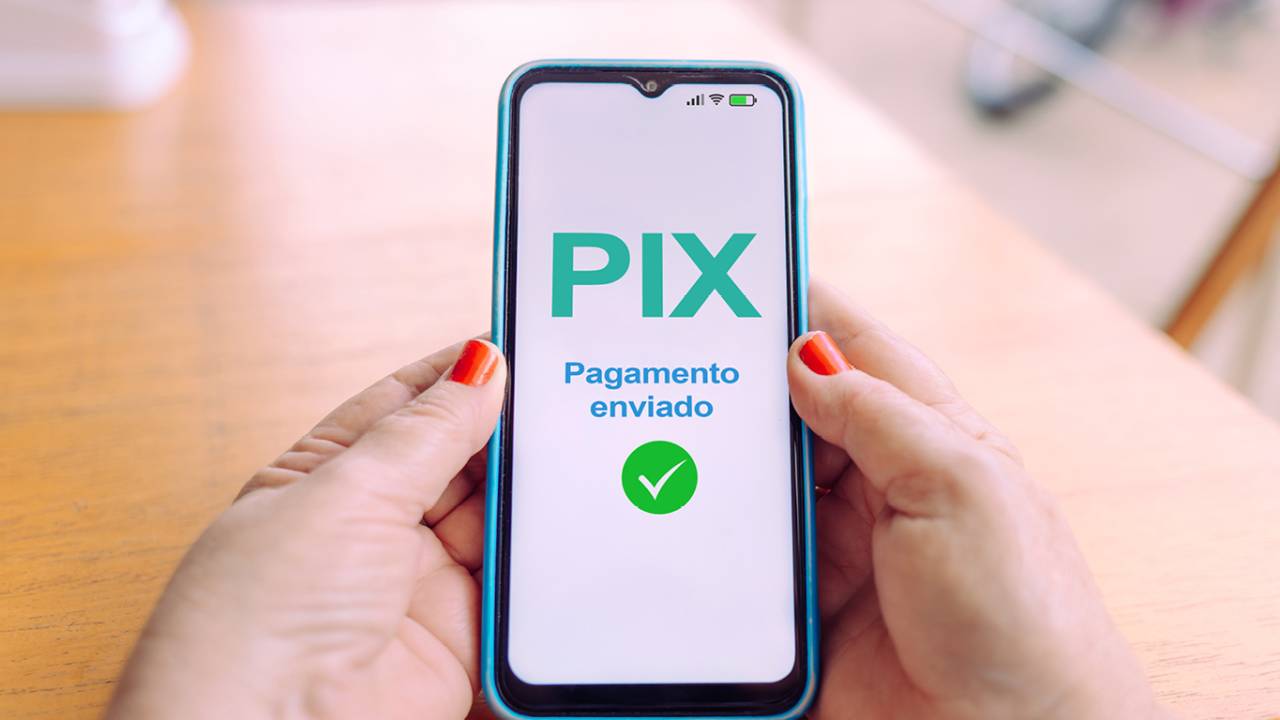 Mãos segurando um smartphone exibindo uma confirmação de pagamento via Pix.