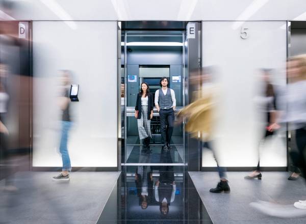 Uma fotografia de pessoas atravessando a porta de um elevador.
